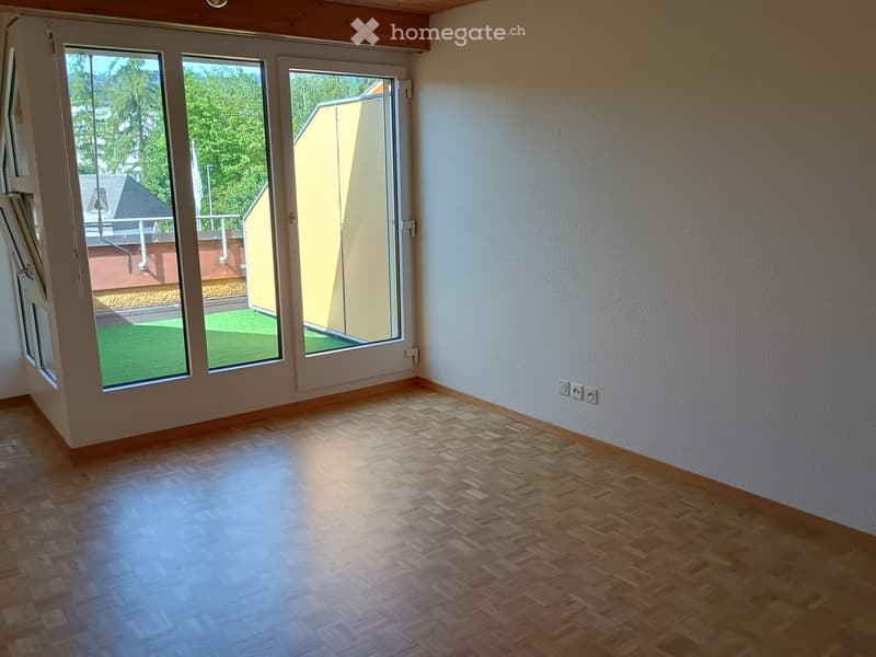Empty room with wooden flooring, large windows, and a sliding glass door leading to a small outdoor area.