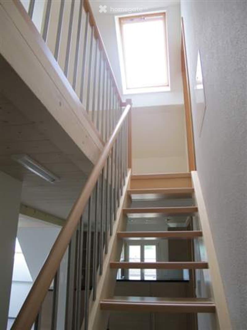 Wooden staircase with a handrail and a window at the top, leading to an upper level.