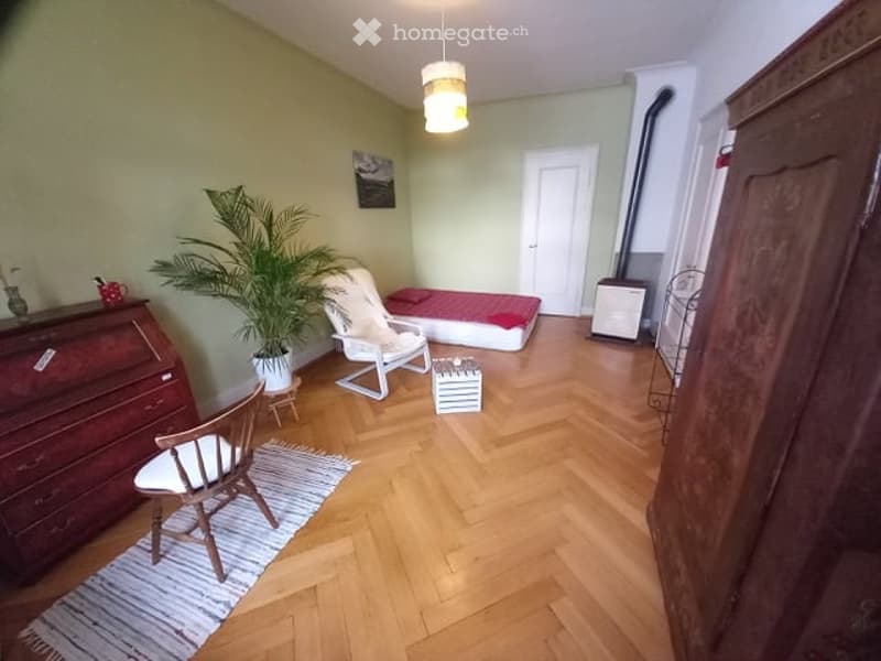 Furnished Room. Cozy, well-furnished room with wooden flooring, a bed, a chair, a small table, a plant, and a wardrobe.