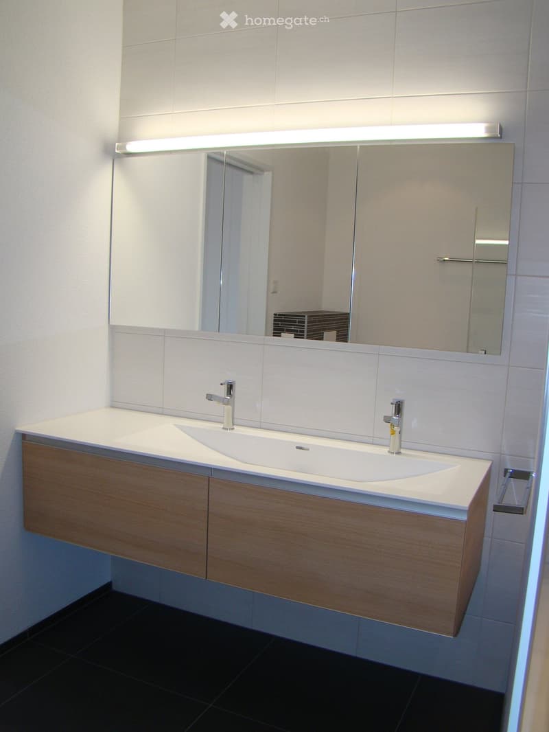 Modern bathroom with a double sink, sleek wooden cabinet, large mirror with built-in lighting, and chrome faucets.