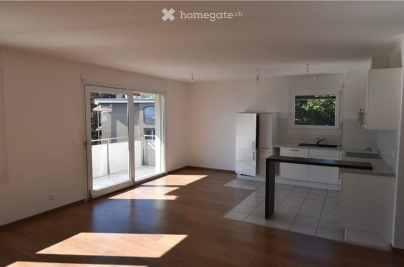 Bright, unfurnished room with wooden flooring, white cabinetry, and a large sliding glass door leading to a balcony.