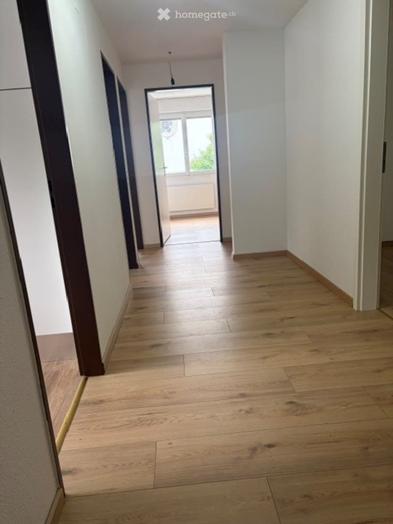 Empty hallway with light wooden flooring, white walls, and a door leading to a balcony or outdoor area.