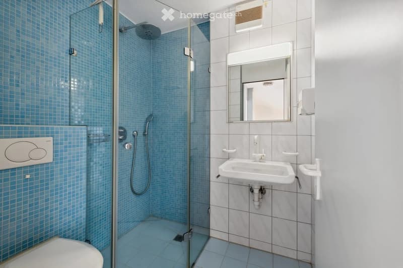 Modern bathroom with blue tiled shower, white toilet, sink, and mirror.