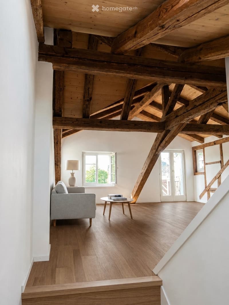 Loft-style living room with exposed wooden beams, hardwood flooring, a grey sofa, a small round coffee table, and a table lamp.