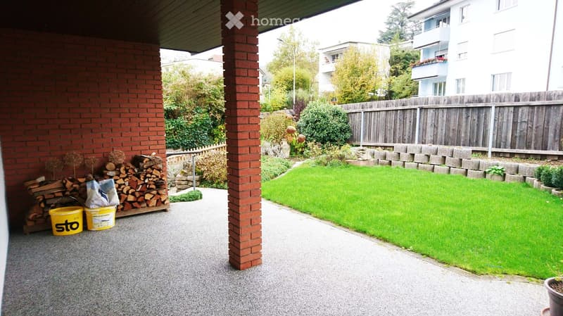 Garden with a well-maintained lawn, wooden fence, brick columns, and a stack of firewood near the entrance.