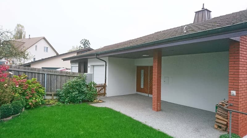 Well-maintained garden with green lawn, wooden fence, and brick house entrance.