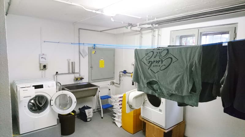 Laundry area with washing machine, dishwasher, sink, and mirror. Clothes are hanging on a line.