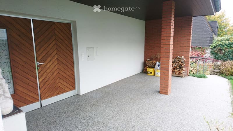 Outdoor patio area with a wooden door, brick columns, stacked firewood, and a yellow bucket.