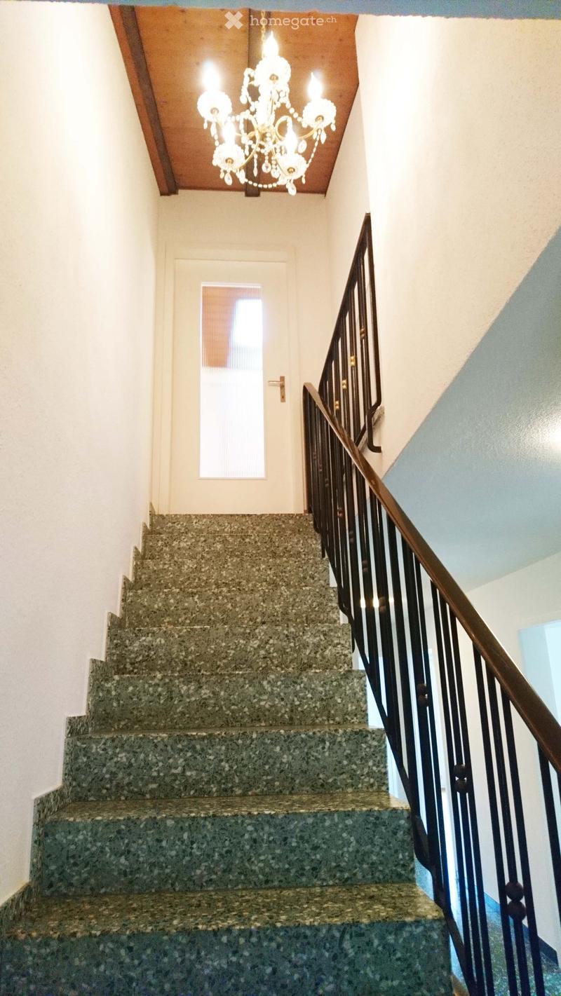 Staircase with granite steps, wooden handrail, and a chandelier hanging from the ceiling.