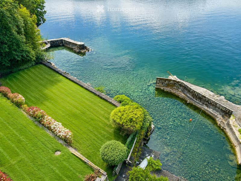 A well-maintained garden with neatly trimmed grass, flower beds, and a stone pathway leading to a dock extending into a calm body of water.