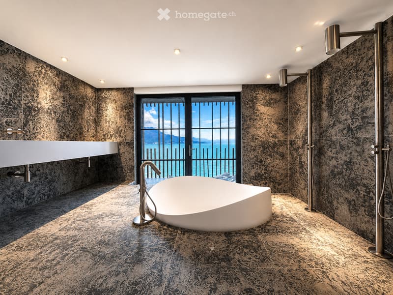 Modern bathroom with dark marble tiles, a freestanding bathtub, a large window offering a scenic view, and sleek metallic fixtures.