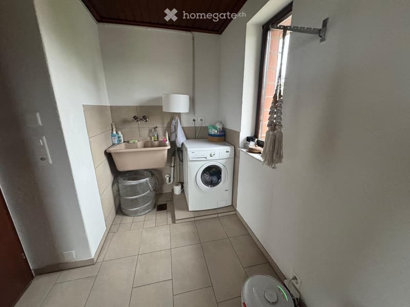 Laundry room with a sink, washing machine, trash can, and a small window.