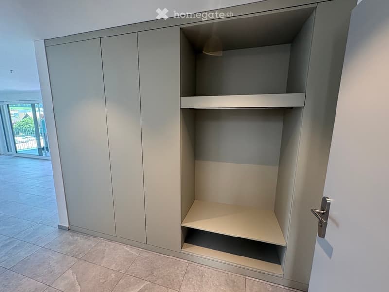 Empty built-in closet with light grey cabinetry and two visible shelves, located in a modern interior with tiled flooring and white walls.
