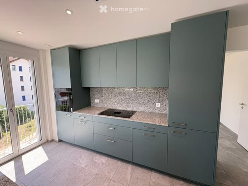 Modern kitchen with grey cabinets, induction cooktop, and a marble countertop. Large window offers a view of the outdoor area.