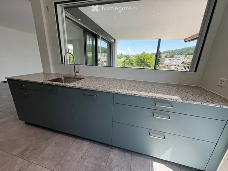 Modern kitchen with grey cabinets, granite countertop, and large windows offering a scenic view.