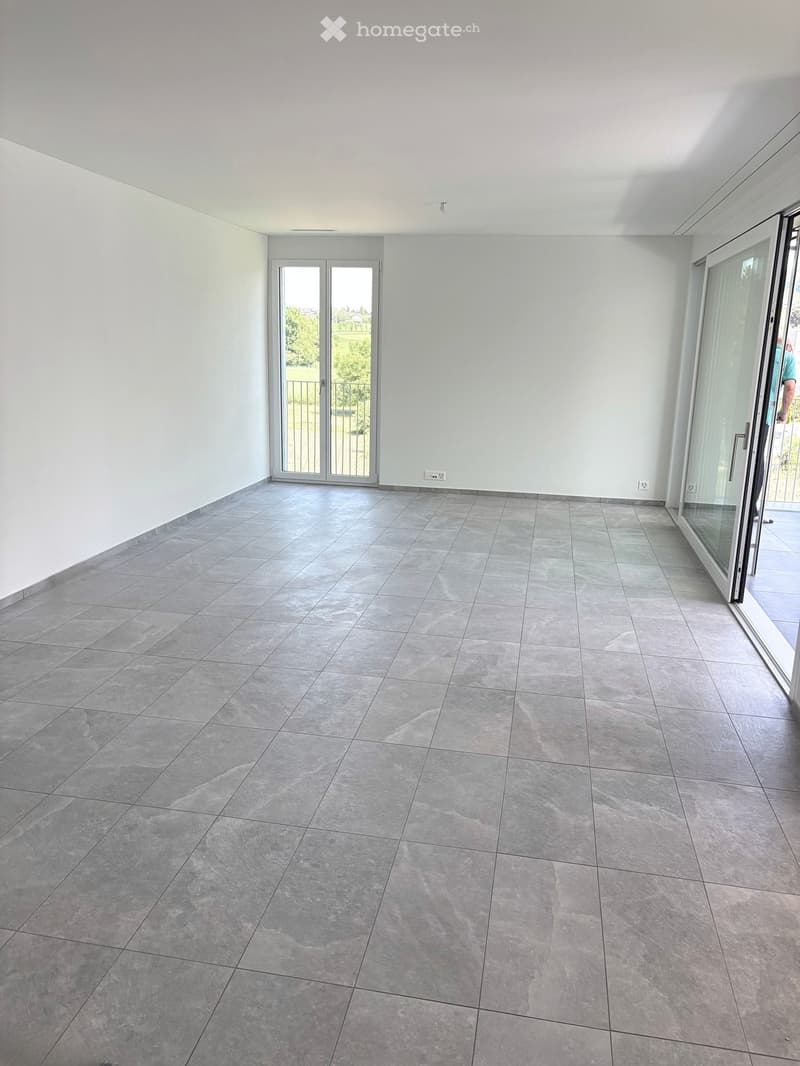 Empty room with grey tiled floor and white walls, featuring two large glass sliding doors leading outside.