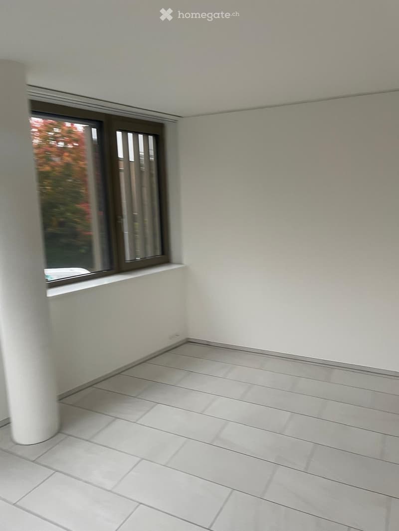 Empty room with white tiled flooring, white walls, and a large window with a view of greenery.