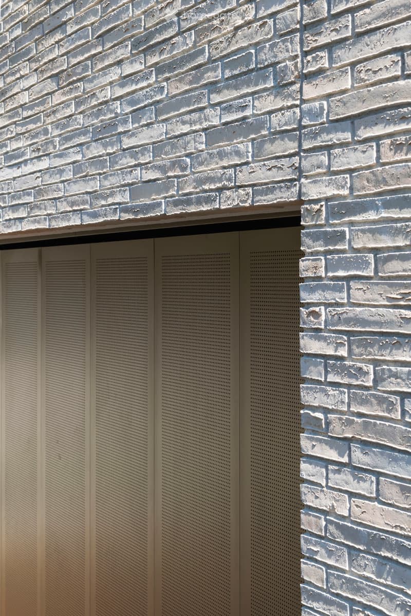 Close-up view of a white brick building facade with perforated metal panels on the lower section.