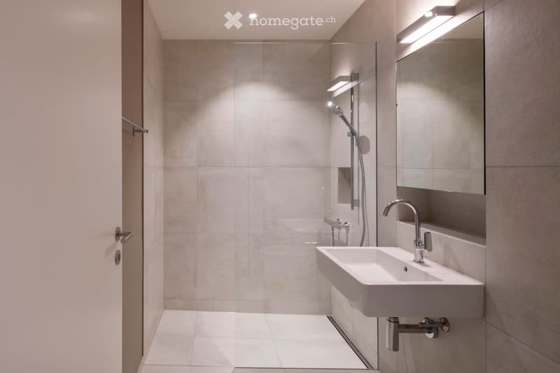 Modern bathroom with a white sink, chrome faucet, large mirror with built-in lighting, and a glass-enclosed shower area with a modern showerhead.