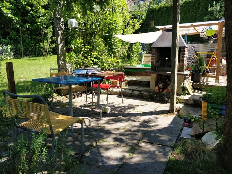Garden area with patio seating, outdoor table, chairs, barbecue, and surrounding greenery.