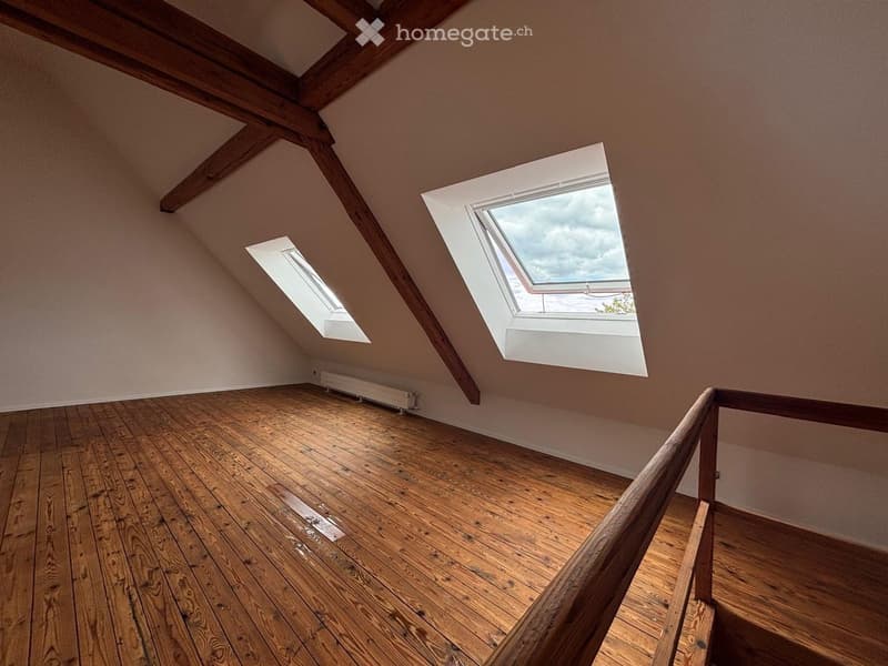 Empty attic room with wooden floors, exposed wooden beams, and skylight windows allowing natural light.