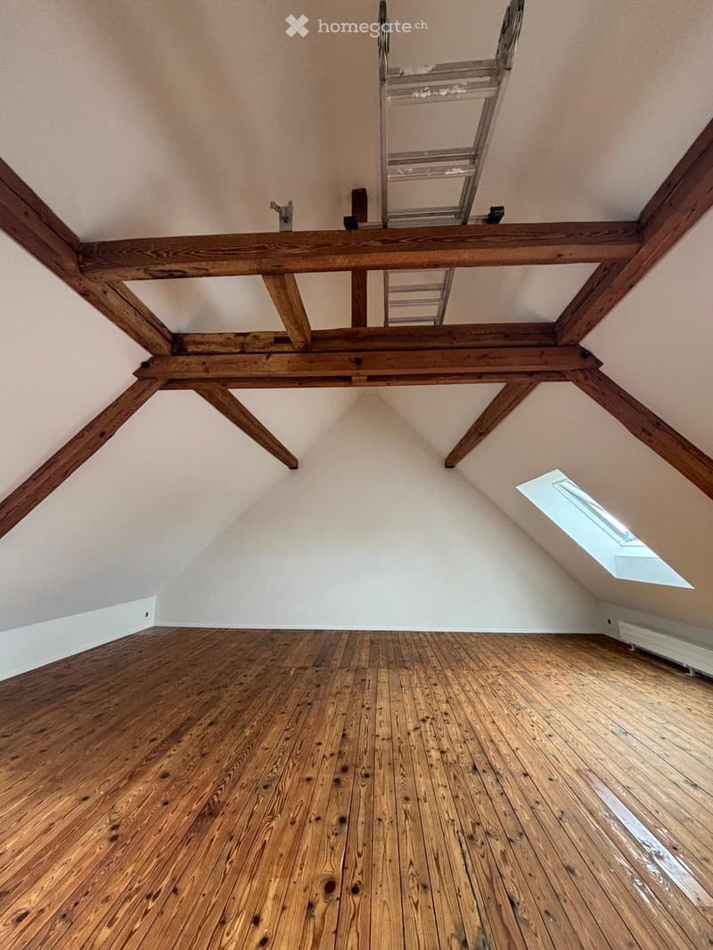 Empty attic space with wooden beams, wooden floor, and a skylight window.