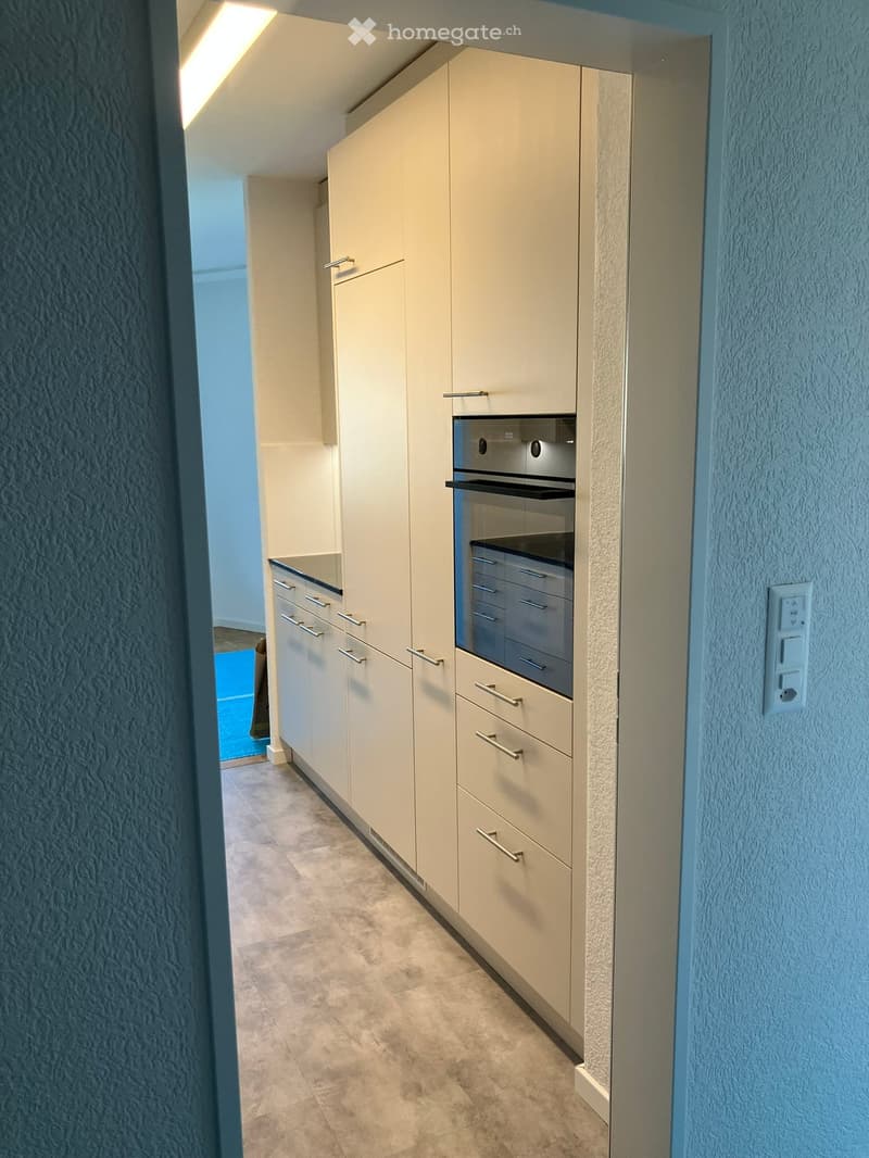 Modern kitchen with light-colored cabinets, stainless steel oven, and tiled floor.
