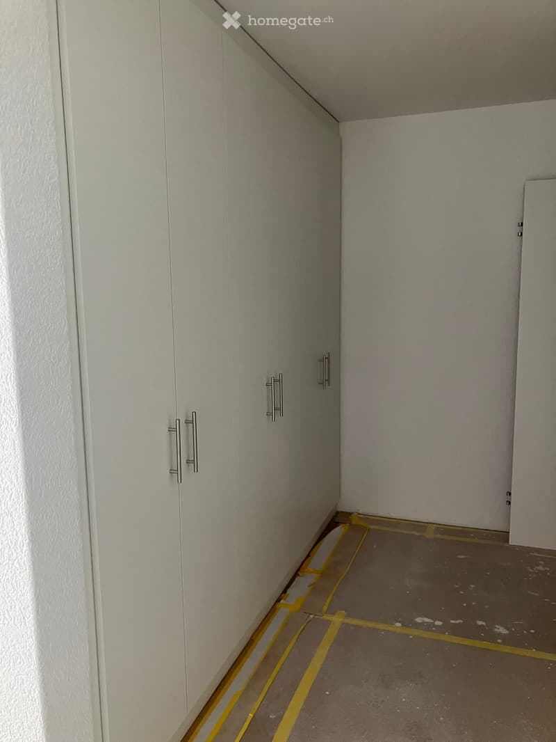 Empty hallway with white walls, grey floor, and yellow tape marking the floor area.