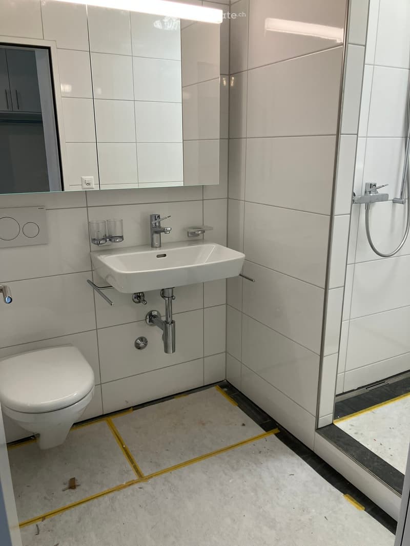 Modern bathroom with white tiles, a toilet, a sink with a chrome faucet, a mirror, and two cups on a shelf.