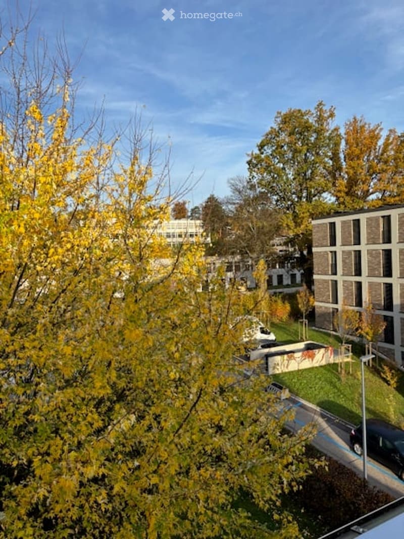 Aerial view of a residential area with an apartment building, several cars parked on the side of the road, and trees in the foreground