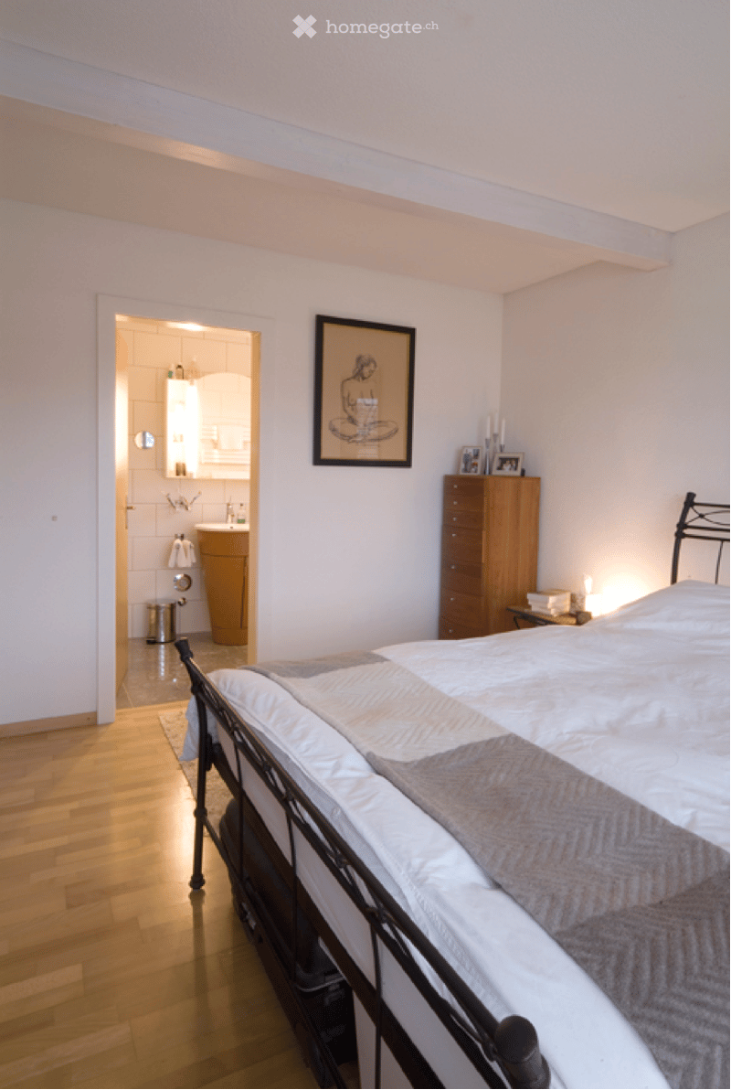 large bed, wooden floor, white walls, wooden cabinet with drawers, picture frame on wall, entrance to bathroom