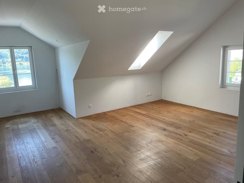 Unfurnished Room. Empty attic room with wooden flooring, white walls, and skylight windows providing natural light.