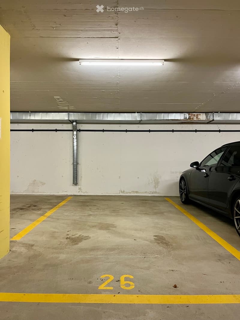 Underground parking space with concrete floor, yellow parking lines, and a parked car in one of the spots.