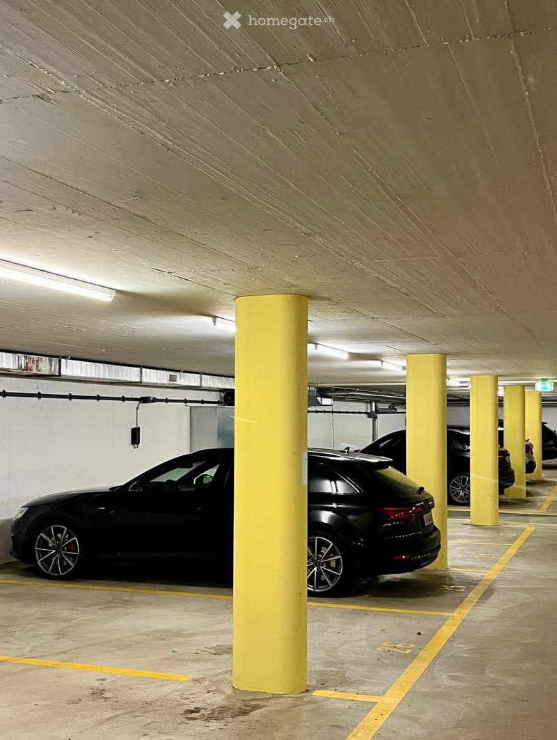 Underground parking area with several parked cars, yellow pillars, and marked parking spaces.