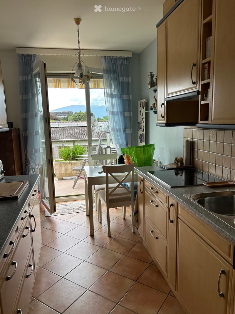 Bright kitchen with tiled floor, light wooden cabinets, and a dining area. Offers a scenic mountain view through large windows and a sliding door leading to a balcony.