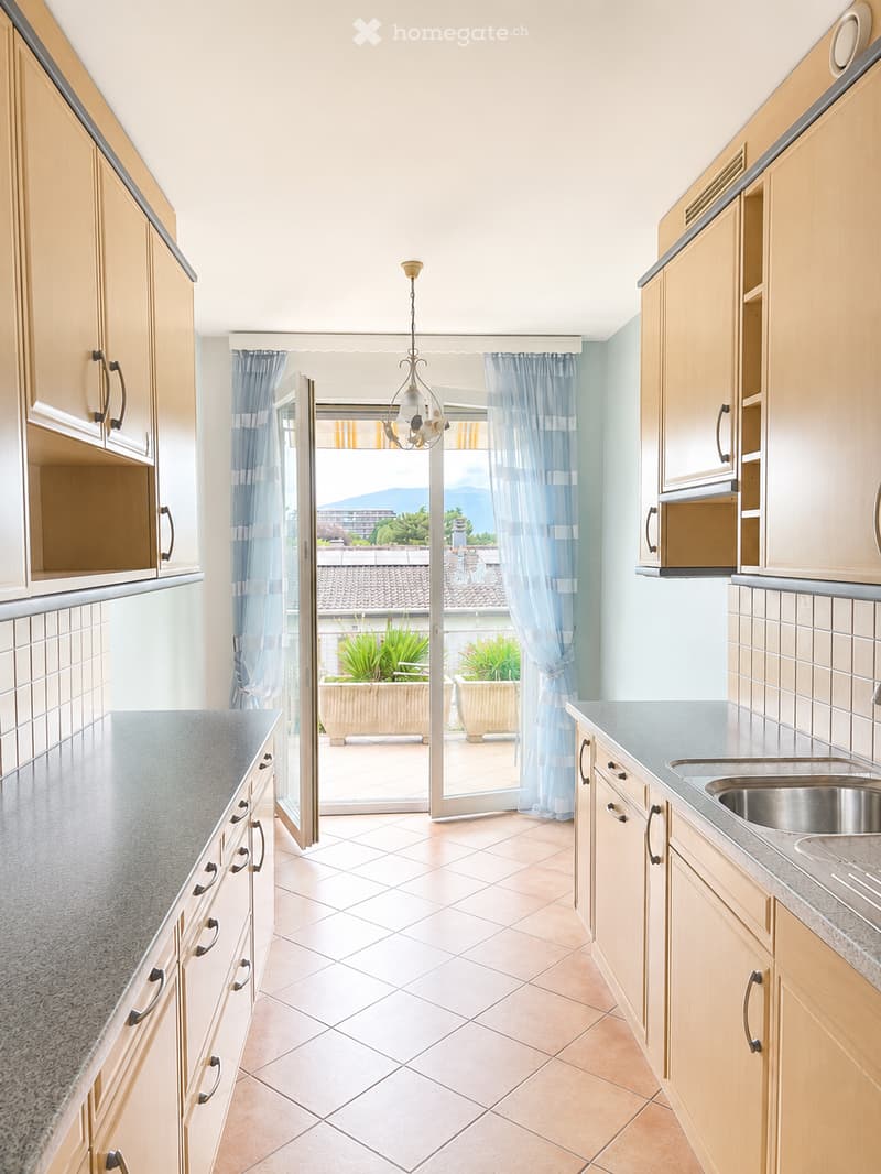 Bright kitchen with light wooden cabinets, granite countertops, and a view of a balcony with potted plants.