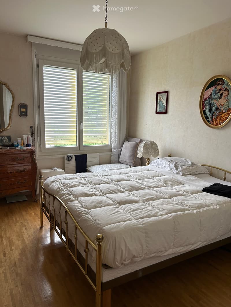 Cozy bedroom with a large bed, nightstand, lamp, mirror, dresser, and framed artwork on the walls.