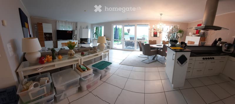 Open-plan living and dining area with a sofa, coffee table, lamps, TV, dining table, chairs, and a modern kitchen with cabinets and a counter.