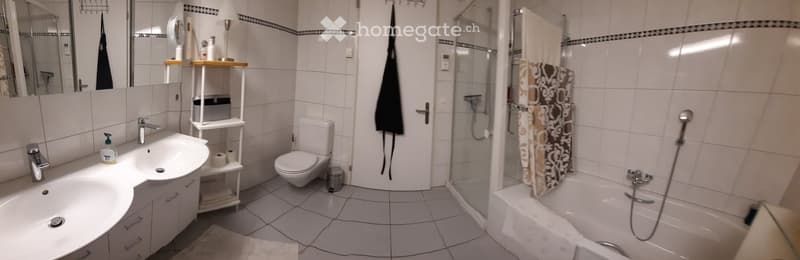 Modern bathroom with white tiles, a sink with a faucet, a toilet, a bathtub with a shower curtain, and a shelf with towels and toiletries.