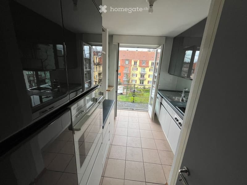 Modern kitchen with white and black cabinets, tiled floor, and a view of a cityscape through a large window. Includes a sink, faucet, oven, and dishwasher.