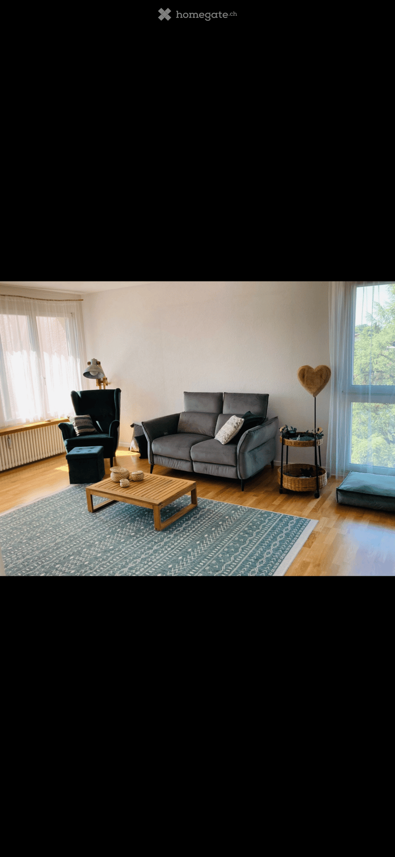 Living room with a couch, coffee table, chair, lamp, rug, and a window with a view of trees