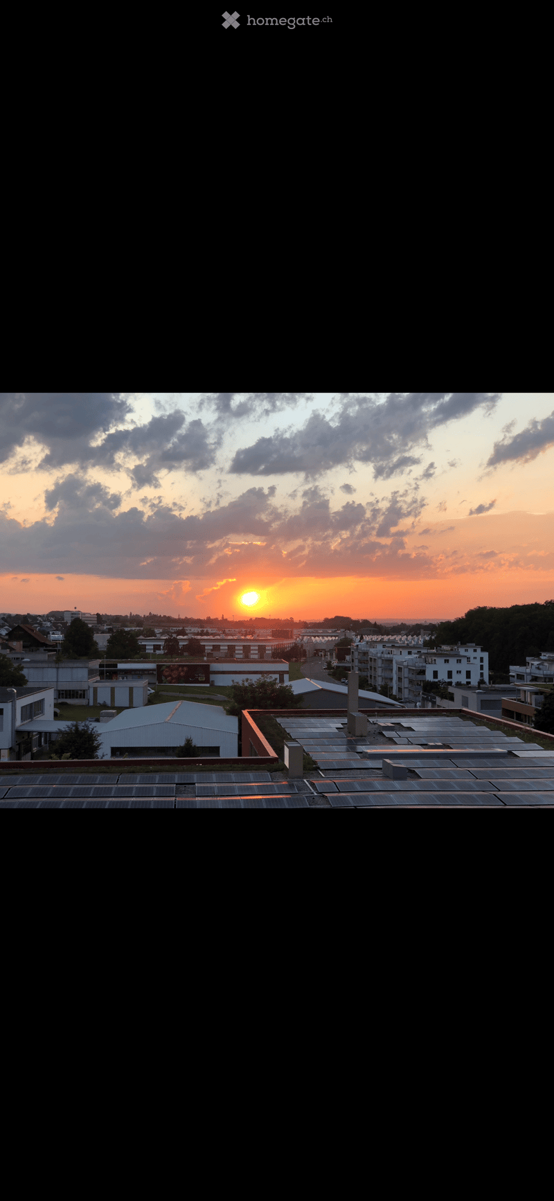 Aerial view of a city with a sunset in the background, solar panels on the rooftop