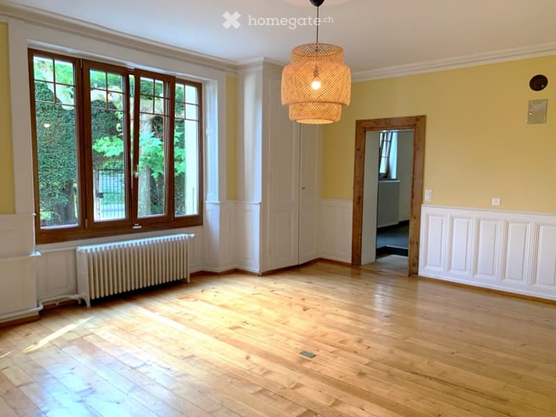 Empty room with wooden flooring, large windows, white walls, and a radiator. No furniture or equipment present.