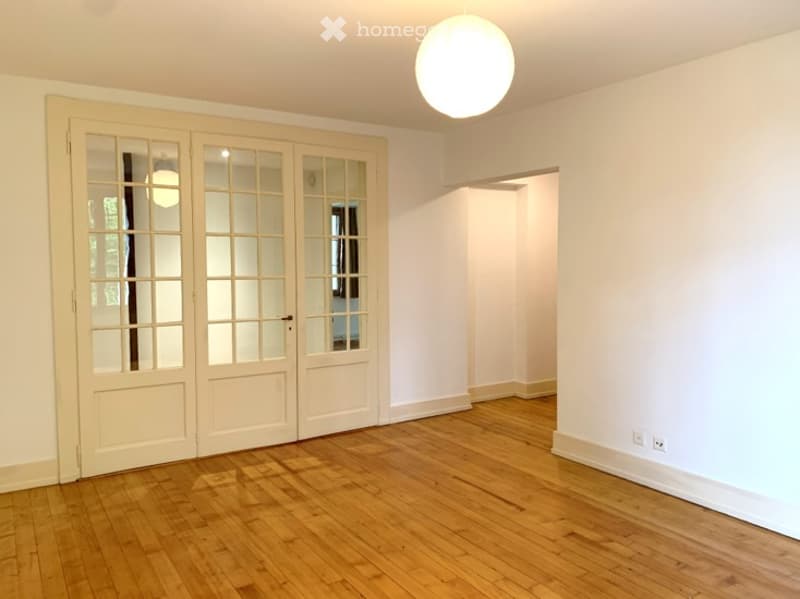 Empty room with wooden flooring, white walls, large glass-paneled doors, and a ceiling light fixture.