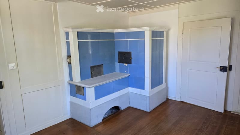 Empty room with wooden flooring, white walls, and a built-in fireplace with blue tiles and a marble shelf.