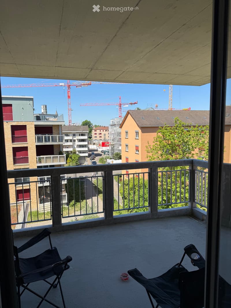Balcony with metal railing, two folding chairs, and a small round object on the floor.