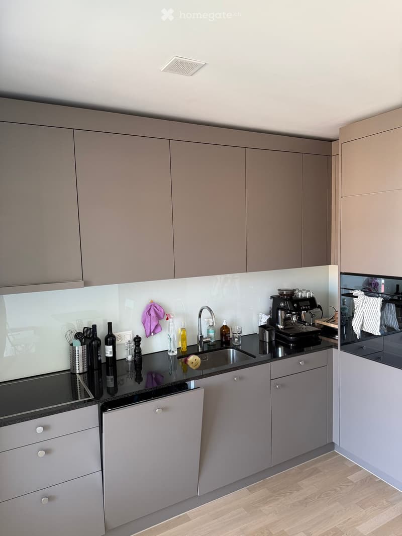 Modern kitchen with grey cabinets, black countertops, stainless steel sink, coffee maker, and various kitchen items on the counter.