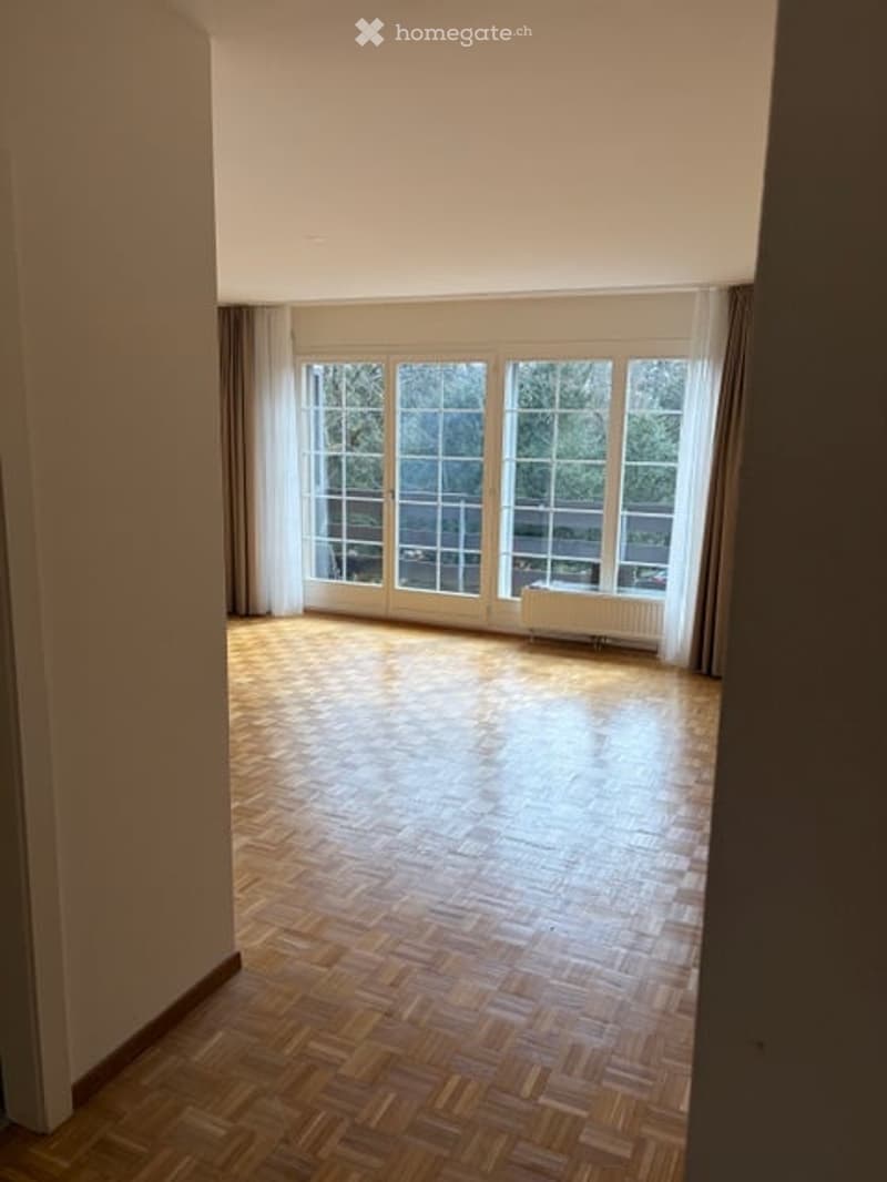 Empty room with wooden flooring, large windows with white frames, and light-colored walls.