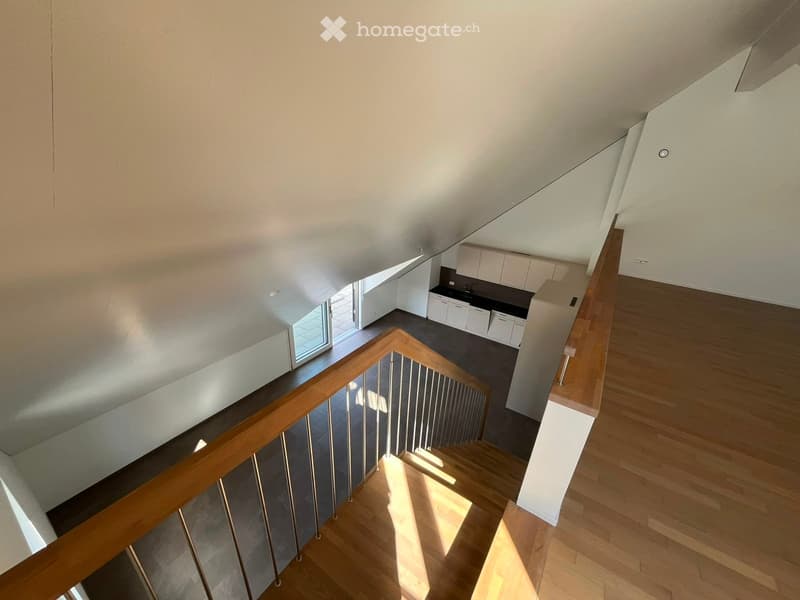 A modern staircase with wooden steps and a metal railing leads down to a kitchen area with white cabinets and a dark countertop.