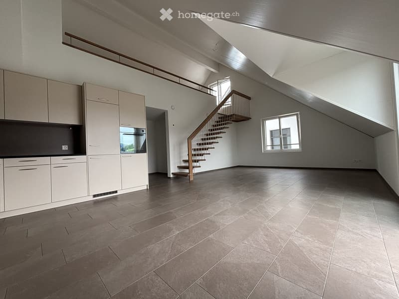Empty room with modern kitchen cabinets, a staircase leading to an upper level, and large windows allowing natural light.